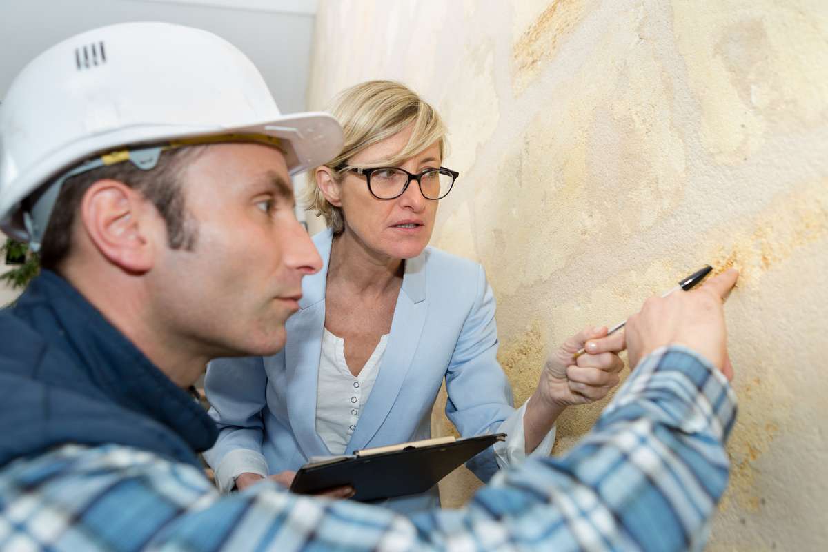 Builder and suited woman inspecting wall (R) (S)