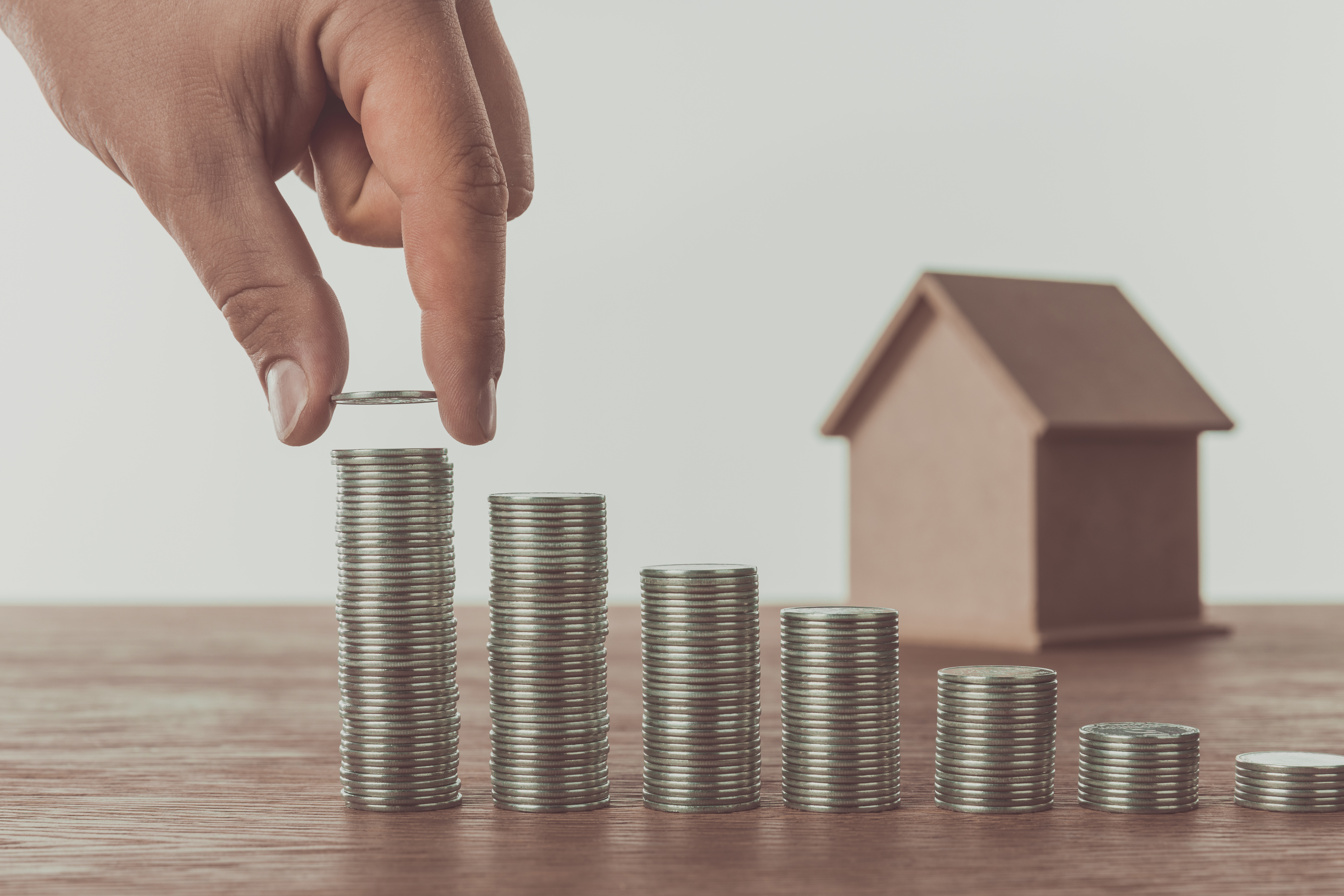 Cropped image of man stacking coins near small house on table, saving concept