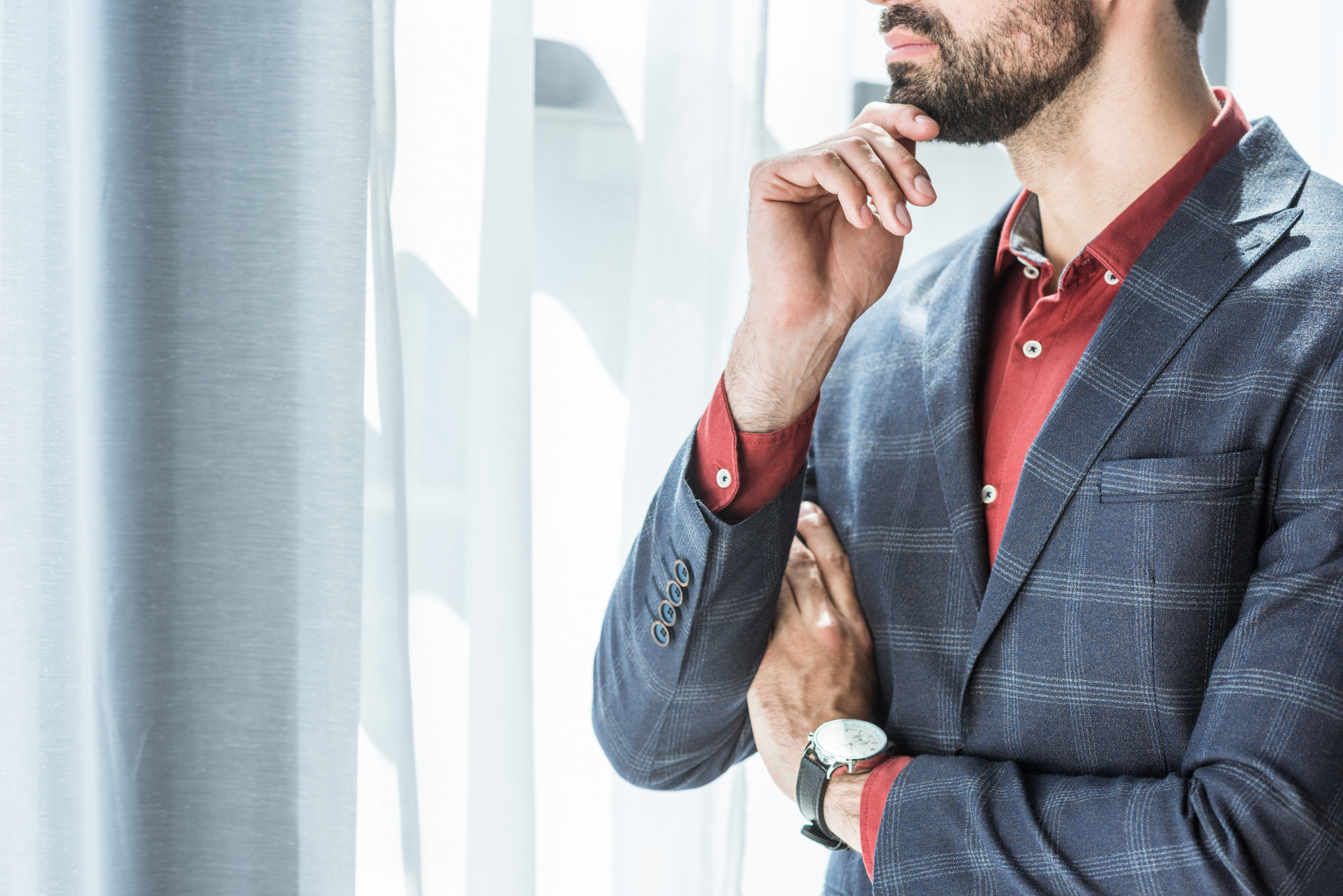 Cropped shot of young businessman with hand on chin looking through window